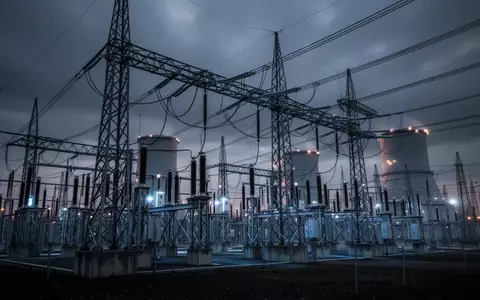 Ein weites, atmosphärisches Foto eines modernen Umspannwerks in der Dämmerung mit komplexen Hochspannungsleitungen und Industriestrukturen unter einem bewölkten Himmel. - Foto: über boerse-global.de