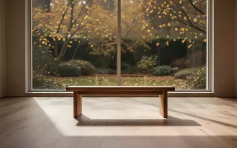Ein minimalistischer, sonnendurchfluteter Raum mit einer hölzernen Meditationsbank und Blick in einen herbstlichen Garten. - Foto: über boerse-global.de