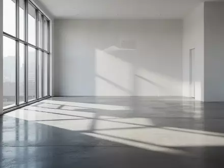 Ein minimalistischer, lichtdurchfluteter Architekturraum mit klaren Linien und geometrischen Schatten auf einem Betonboden. - Foto: über boerse-global.de