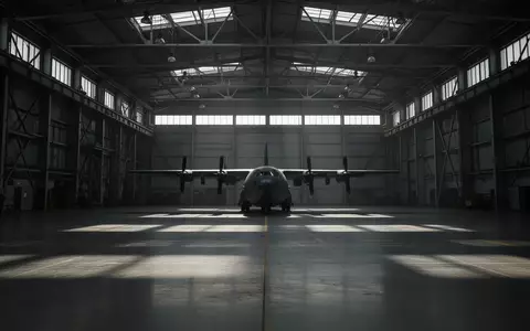 Eine weitläufige, menschenleere Flugzeughalle mit einem im Schatten stehenden Militärflugzeug und einfallendem Tageslicht. - Foto: über boerse-global.de