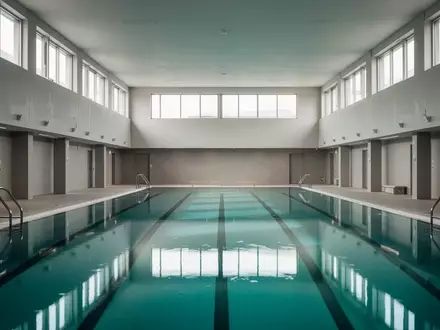 Ein leeres, modernes Schwimmbecken in einer lichtdurchfluteten Sporthalle mit klaren architektonischen Linien. - Foto: über boerse-global.de