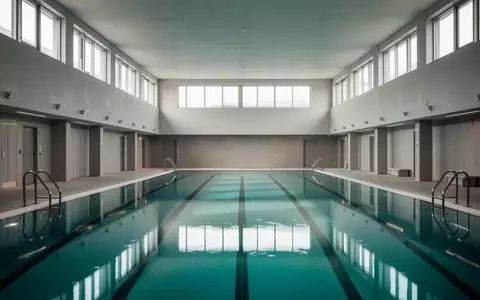 Ein leeres, modernes Schwimmbecken in einer lichtdurchfluteten Sporthalle mit klaren architektonischen Linien. - Foto: über boerse-global.de