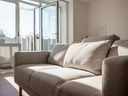 Ein helles, modern eingerichtetes Wohnzimmer mit Fokus auf die Textur eines Polstersofas bei natürlichem Lichteinfall. - Foto: über boerse-global.de