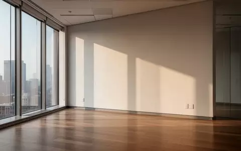 Ein minimalistischer, leerer Büroraum mit hellem, natürlichem Lichteinfall durch große Fenster auf einen Holzboden. - Foto: über boerse-global.de