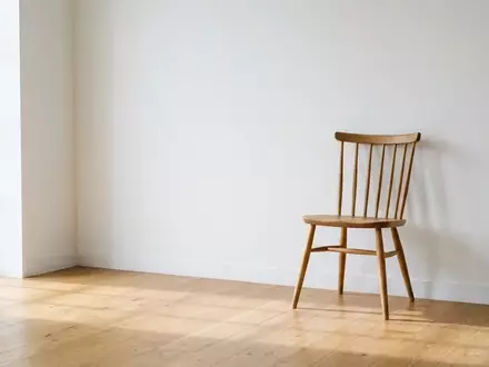 Ein leerer Holzstuhl in einem minimalistisch eingerichteten, sonnendurchfluteten Raum vor einer weißen Wand. - Foto: über boerse-global.de