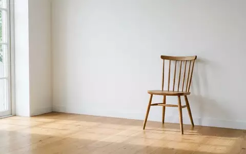 Ein leerer Holzstuhl in einem minimalistisch eingerichteten, sonnendurchfluteten Raum vor einer weißen Wand. - Foto: über boerse-global.de