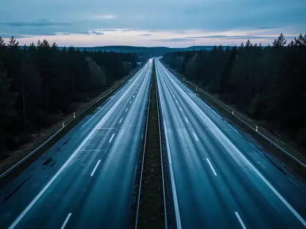 Leere, nasse Autobahn bei Dämmerung in einer bewaldeten Landschaft. - Foto: über boerse-global.de