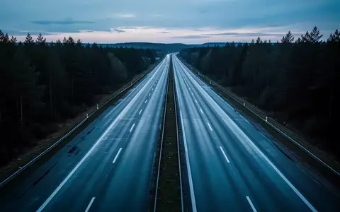 Leere, nasse Autobahn bei Dämmerung in einer bewaldeten Landschaft. - Foto: über boerse-global.de