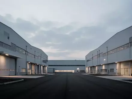 Weite Ansicht eines modernen, menschenleeren Industrieparks bei Dämmerung mit großen Fabrikhallen vor einem bewölkten Himmel. - Foto: über boerse-global.de