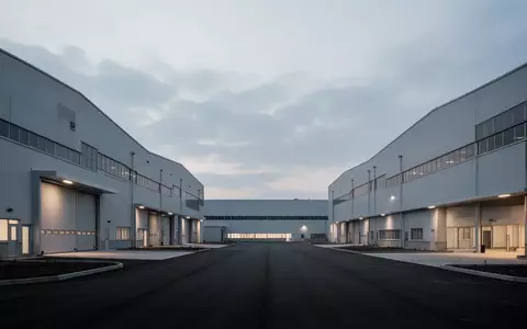 Weite Ansicht eines modernen, menschenleeren Industrieparks bei Dämmerung mit großen Fabrikhallen vor einem bewölkten Himmel. - Foto: über boerse-global.de