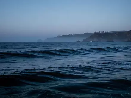 Weite, tiefblaue Meeresoberfläche bei Dämmerung mit sanften Wellen und der vagen Silhouette einer Küste am Horizont. - Foto: über boerse-global.de