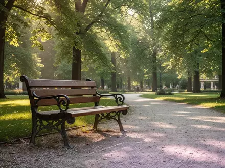 Eine leere, hölzerne Parkbank auf einem Kiesweg im Grazer Augarten an einem sonnigen Nachmittag. - Foto: über boerse-global.de