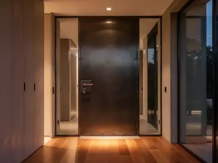 Ein moderner, minimalistischer Hauseingang mit einer soliden Metalltür in einer warm beleuchteten Wohnung. - Foto: über boerse-global.de