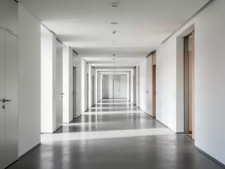 Heller, minimalistischer Flur in einem modernen Verwaltungsgebäude mit klaren architektonischen Linien und Tageslicht. - Foto: über boerse-global.de