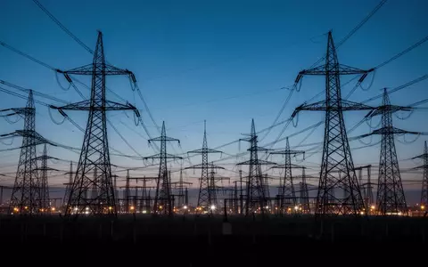 Hochspannungsmasten und industrielle Infrastruktur in einer weitläufigen Landschaft bei Dämmerung. - Foto: über boerse-global.de