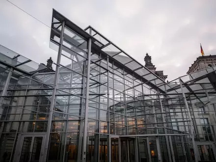 Moderne Glas- und Stahlfassade des Berliner Reichstagsgebäudes vor einem bewölkten Himmel. - Foto: über boerse-global.de