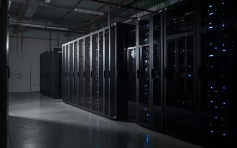 Ein dunkler, minimalistischer Serverraum mit leuchtenden Status-LEDs an metallischen Schaltschränken in einer Industriehalle. - Foto: über boerse-global.de