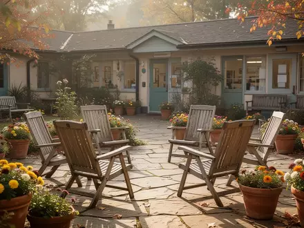 Ein sonniger Innenhof eines Gemeindezentrums mit in einem Kreis aufgestellten Gartenstühlen und herbstlichen Blumenkübeln. - Foto: über boerse-global.de