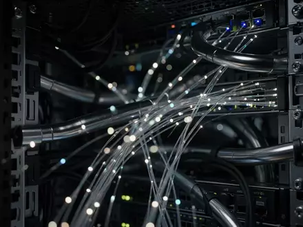 Dunkle Server-Infrastruktur mit leuchtenden Glasfaserkabeln und metallischen Leitungen in einer industriellen Umgebung. - Foto: über boerse-global.de
