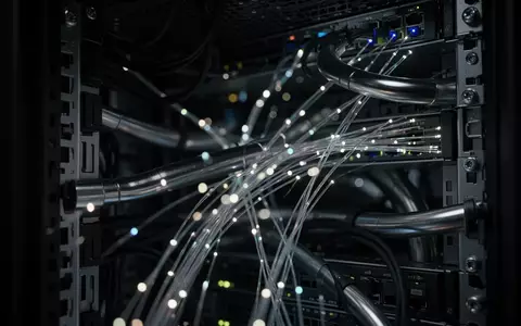 Dunkle Server-Infrastruktur mit leuchtenden Glasfaserkabeln und metallischen Leitungen in einer industriellen Umgebung. - Foto: über boerse-global.de
