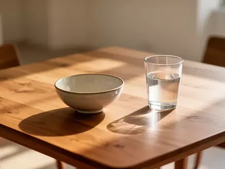 Ein minimalistischer Holztisch mit einer leeren Keramikschale und einem Glas Wasser in natürlichem Morgenlicht. - Foto: über boerse-global.de