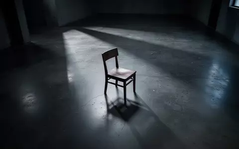 Ein leerer Holzstuhl in einem minimalistischen Raum mit langen Schatten auf einem Betonboden, der die Atmosphäre von finanzieller Verletzlichkeit unterstreicht. - Foto: über boerse-global.de