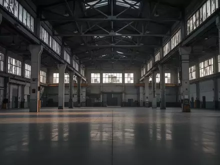 Eine leere, weitläufige Industriehalle mit Betonpfeilern und Stahlträgern bei Dämmerlicht. - Foto: über boerse-global.de
