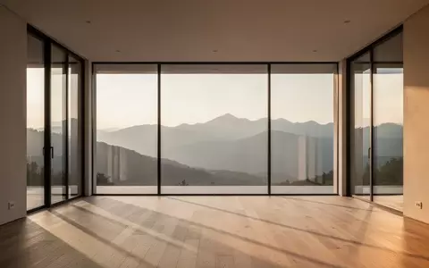 Ein minimalistisch gestalteter, leerer Raum mit bodentiefen Fenstern und Blick auf eine weite Berglandschaft bei Sonnenuntergang. - Foto: über boerse-global.de