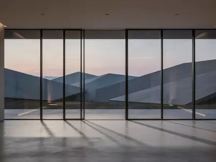 Ein minimalistisch gestalteter Innenraum mit bodentiefen Fenstern und Blick auf eine abstrakte Landschaft bei Dämmerung. - Foto: über boerse-global.de