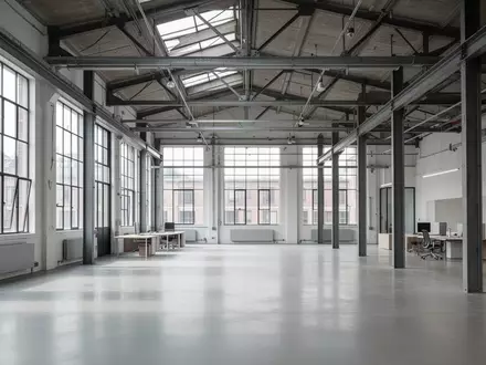 Ein minimalistischer, moderner Arbeitsbereich in einem renovierten Fabrikgebäude mit hohen Decken und natürlichem Lichteinfall. - Foto: über boerse-global.de