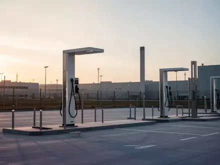 Moderne Ladesäulen auf einem leeren, weitläufigen Industriegelände bei Dämmerung. - Foto: über boerse-global.de