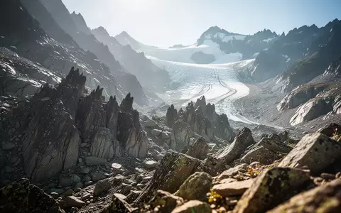 Eine raue, sonnenbeschienene Hochgebirgslandschaft mit zerklüfteten Felsen und einem Gletscher im Hintergrund. - Foto: über boerse-global.de