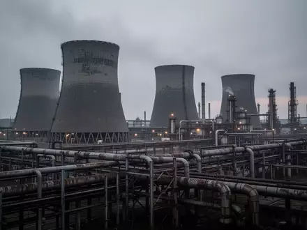 Ein weitläufiger Industriepark mit Kühltürmen und Rohrleitungssystemen unter einem grauen Himmel. - Foto: über boerse-global.de