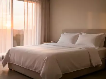 Ein minimalistisch eingerichtetes Schlafzimmer in den frühen Morgenstunden mit weichem Tageslicht und ordentlich gemachtem Bett. - Foto: über boerse-global.de