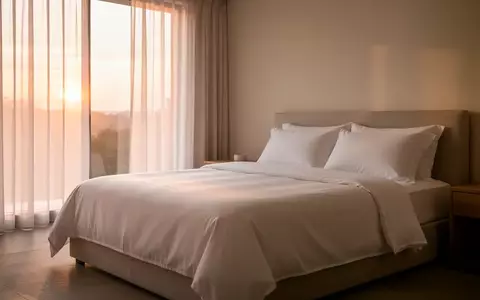 Ein minimalistisch eingerichtetes Schlafzimmer in den frühen Morgenstunden mit weichem Tageslicht und ordentlich gemachtem Bett. - Foto: über boerse-global.de