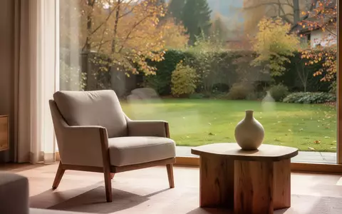 Ein ruhiges, sonnendurchflutetes Wohnzimmer mit einem Sessel und Blick in einen herbstlichen Garten, das eine friedliche Atmosphäre vermittelt. - Foto: über boerse-global.de