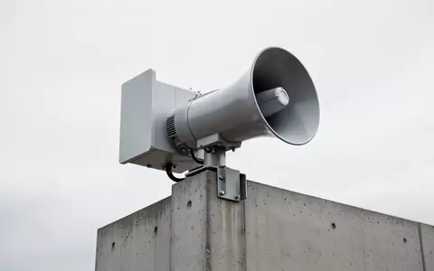 Eine moderne Notfallsirene auf einem Betonmast vor einem bewölkten Himmel. - Foto: über boerse-global.de