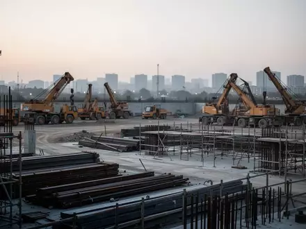 Leere Baustelle in der Dämmerung mit schweren Baumaschinen und Stahlgerüsten vor einem urbanen Hintergrund. - Foto: über boerse-global.de