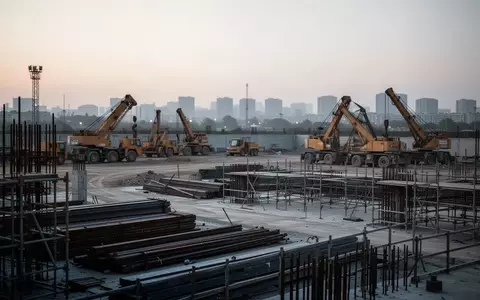 Leere Baustelle in der Dämmerung mit schweren Baumaschinen und Stahlgerüsten vor einem urbanen Hintergrund. - Foto: über boerse-global.de