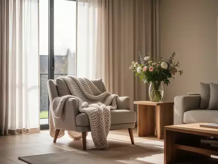Ein helles, ruhiges Wohnzimmer mit einem bequemen Sessel und frischen Blumen, das eine Atmosphäre häuslicher Geborgenheit vermittelt. - Foto: über boerse-global.de