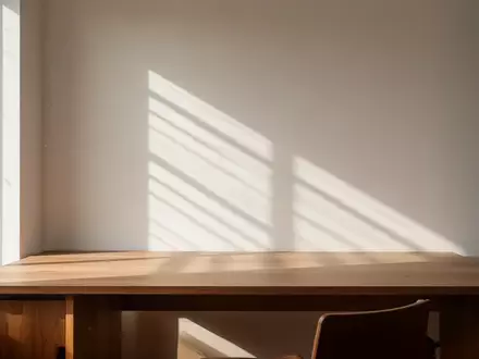 Ein minimalistischer, sonnendurchfluteter Arbeitsplatz mit einem leeren Holztisch und weichen Schatten an der Wand. - Foto: über boerse-global.de