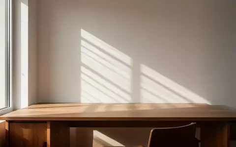 Ein minimalistischer, sonnendurchfluteter Arbeitsplatz mit einem leeren Holztisch und weichen Schatten an der Wand. - Foto: über boerse-global.de