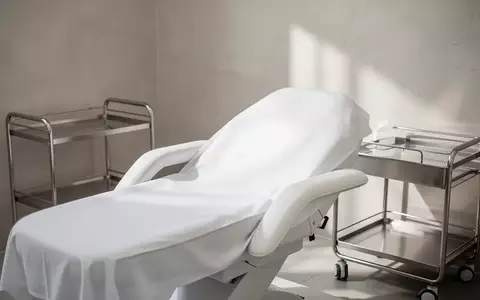 Ein minimalistisch eingerichteter, steriler Behandlungsraum in einer Klinik mit einer Liege und neutralen Wandtexturen. - Foto: über boerse-global.de