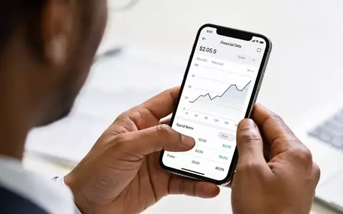 Nahaufnahme einer Hand, die ein Smartphone mit Finanzdiagrammen in einer professionellen Büroumgebung hält. - Foto: über boerse-global.de