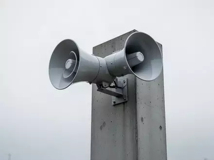 Eine moderne, minimalistische Notfallsirene auf einem Betonmast vor einem bewölkten Himmel. - Foto: über boerse-global.de