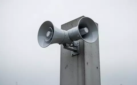 Eine moderne, minimalistische Notfallsirene auf einem Betonmast vor einem bewölkten Himmel. - Foto: über boerse-global.de