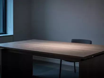 Ein minimalistischer, leerer Schreibtisch in einem abgedunkelten, modernen Raum mit sanftem, bläulichem Licht. - Foto: über boerse-global.de