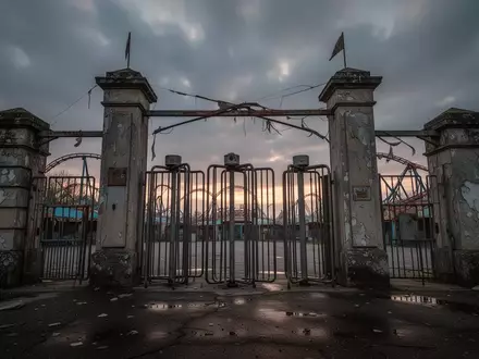 Leere Eingangstore eines Freizeitparks bei Dämmerung mit Drehkreuzen aus Eisen vor einem bewölkten Himmel. - Foto: über boerse-global.de