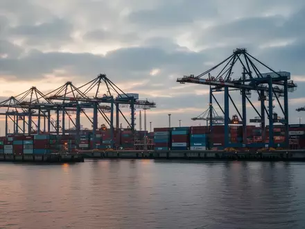 Industrielles Hafengelände in Hamburg mit Containern und Kränen bei Dämmerung als Symbol für kritische Infrastruktur. - Foto: über boerse-global.de