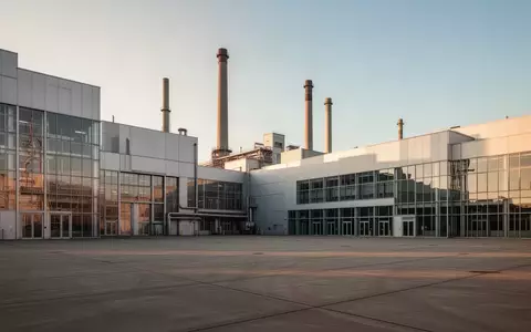 Weitwinkelaufnahme einer großen Industrieanlage bei Sonnenuntergang mit moderner Architektur und weitem Vorplatz. - Foto: über boerse-global.de